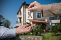Person with a blue shirt sleeve reaching out as a person with a tan shirt sleeve hands them a pair of keys to a home