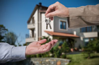 Person with a blue shirt sleeve reaching out as a person with a tan shirt sleeve hands them a pair of keys to a home